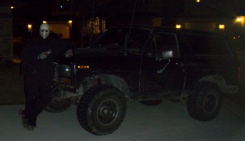1985 Ford Bronco - A person in a mask poses next to a black 1985 Ford Bronco at night.