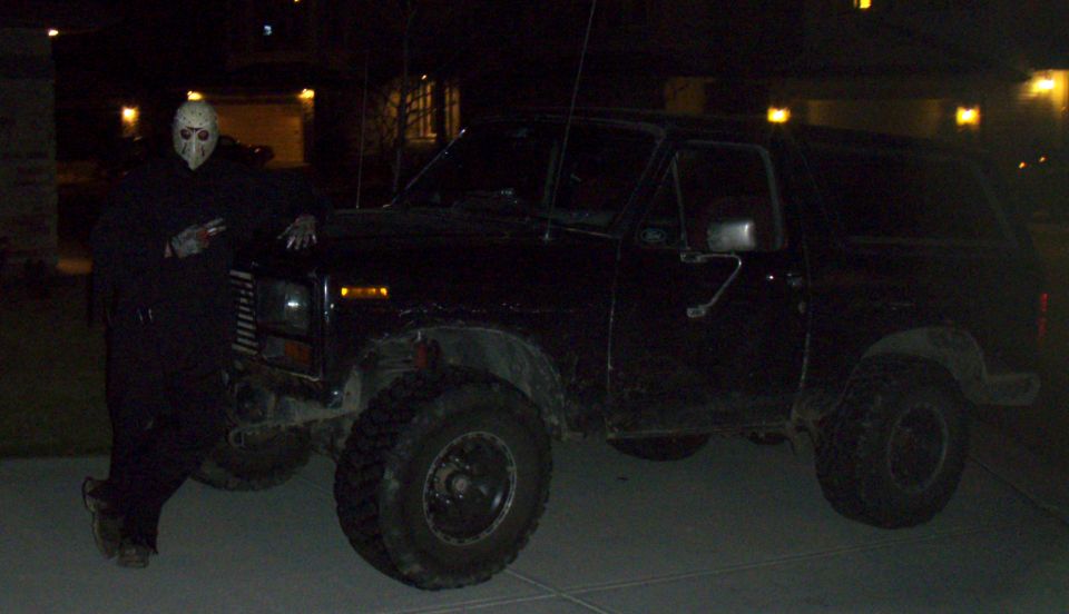 Black 1985 Ford Bronco with person in mask