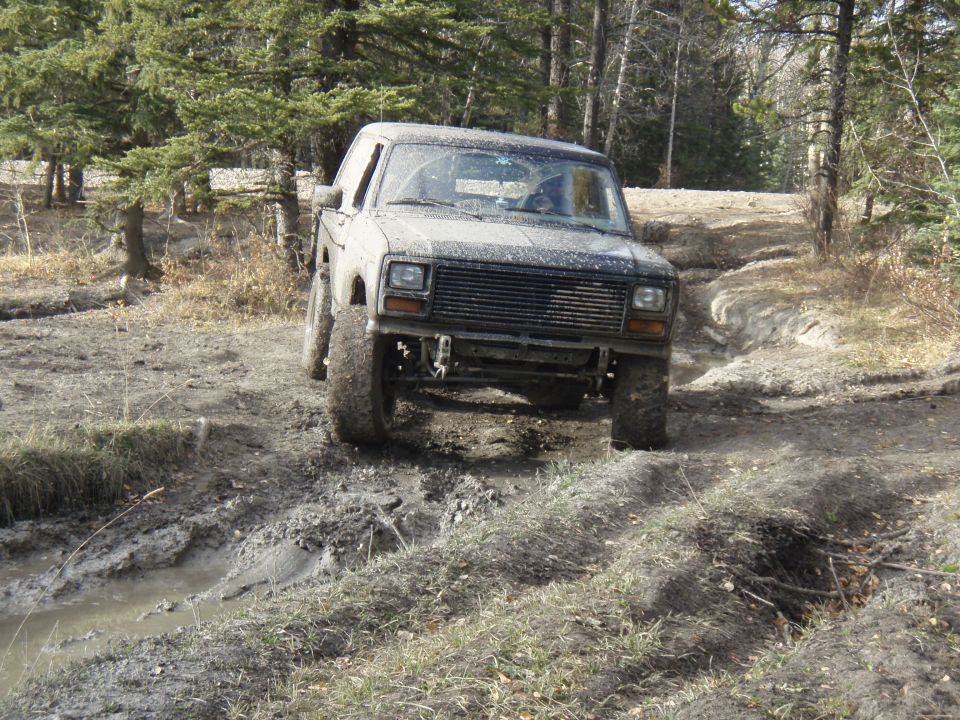Muddy 1980s 4x4 truck navigating a dirt track with trees in background