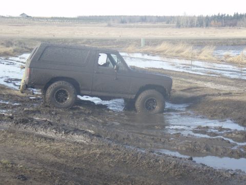 1985 Ford Bronco - This SUV is covered in mud while navigating a challenging off-road terrain.