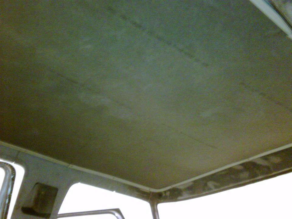 Interior ceiling of a vehicle, showing a textured green headliner with visible seams and some discoloration. The edges reveal structural components