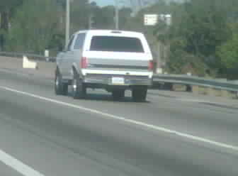1986 Ford Bronco - A white Ford Bronco is seen driving on a highway during the day.