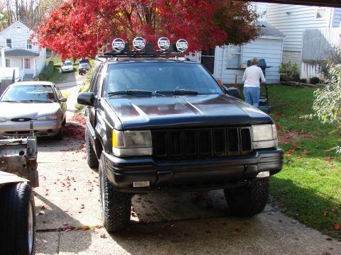 1996 Jeep Grand Cherokee - A black 1996 Jeep Grand Cherokee is parked in a driveway with a Ford Taurus and other vehicles nearby.
