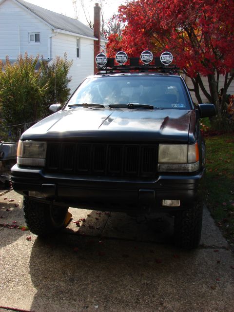1996 Jeep Grand Cherokee - A black 1996 Jeep Grand Cherokee is shown from the front, equipped with a roof rack and four Hella lights.