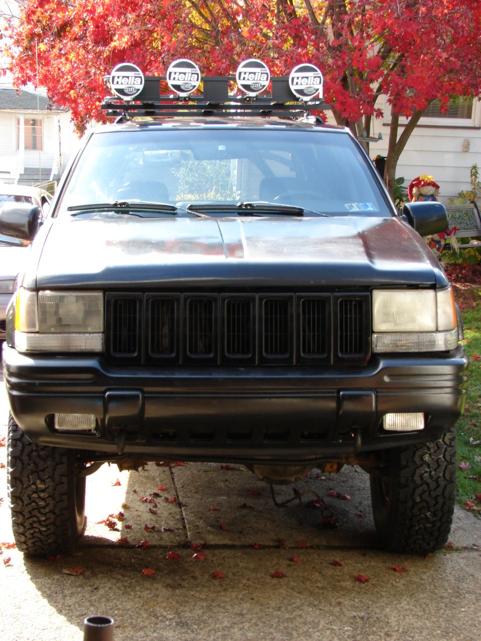 1996 Jeep Grand Cherokee front view, black paint, roof rack with four Hella lights, autumn foliage in background