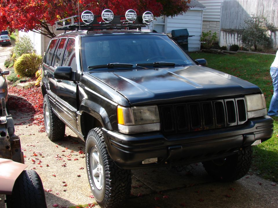 Black Jeep Grand Cherokee with roof lights and off-road tires parked outside
