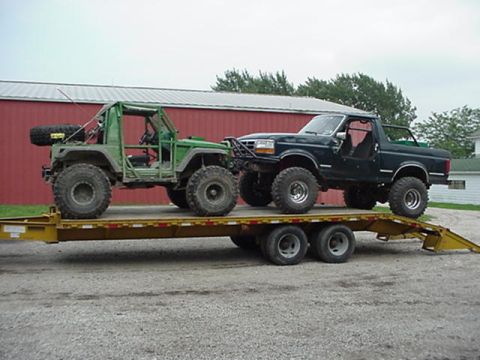 1992 Ford Bronco - Two modified off-road vehicles are loaded onto a flatbed trailer.