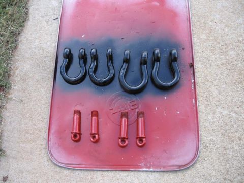 1995 Ford F-150 - Six black tow hooks and four red bolts are laid out on a red surface with black spray paint.