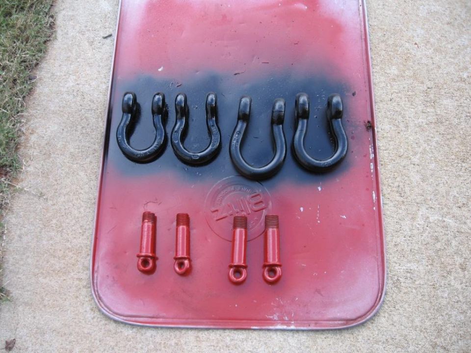 Red painted surface with black spray paint overspray, holding six black U-shaped tow hooks and four red bolts