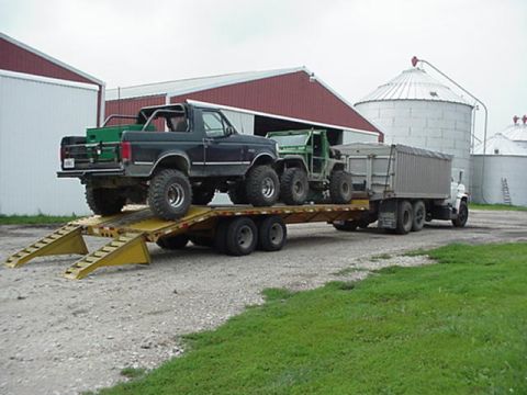 1992 Ford Bronco - A black 1992 Ford Bronco and a green utility vehicle are loaded onto a trailer, with farm buildings in the background.