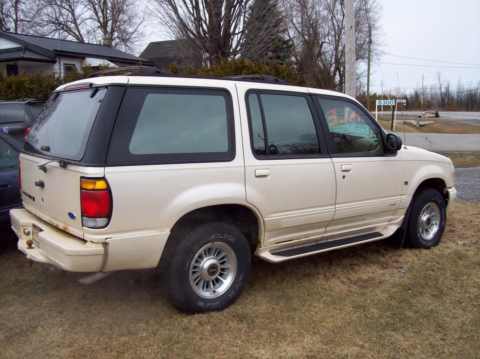 Beige 1990s Ford Explorer SUV, rear three-quarter view, with SALE painted on the window