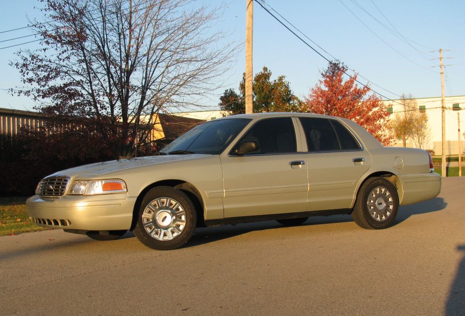 Gold Ford Crown Victoria sedan front three-quarter view on pavement at sunset