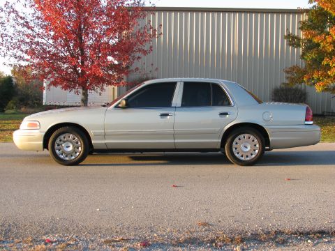 2004 Ford Crown Victoria - A silver sedan is parked on a road with a building and trees in the background.