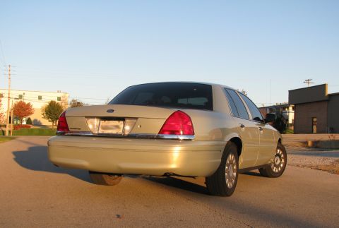 2004 Ford Crown Victoria - This tan sedan is seen from a rear three-quarter angle under a clear sky.