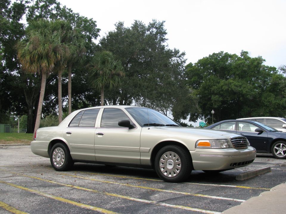 Gold Ford Crown Victoria sedan parked in lot, passenger front 3/4 view