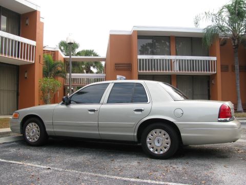 2004 Ford Crown Victoria - A silver sedan is parked in a lot with buildings and palm trees in the background.
