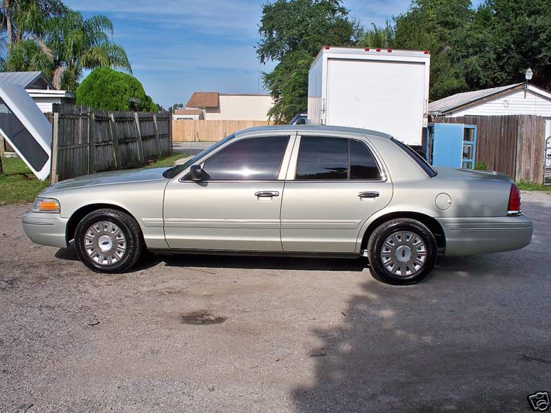 Champagne gold Ford Crown Victoria sedan driver-side profile on paved lot