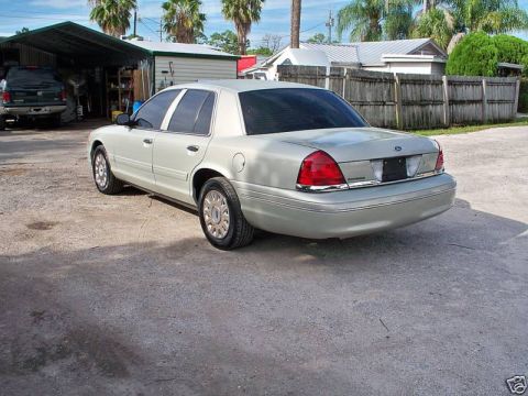 2004 Ford Crown Victoria - A light-colored Ford Crown Victoria is parked on a gravel lot with a wooden fence in the background.