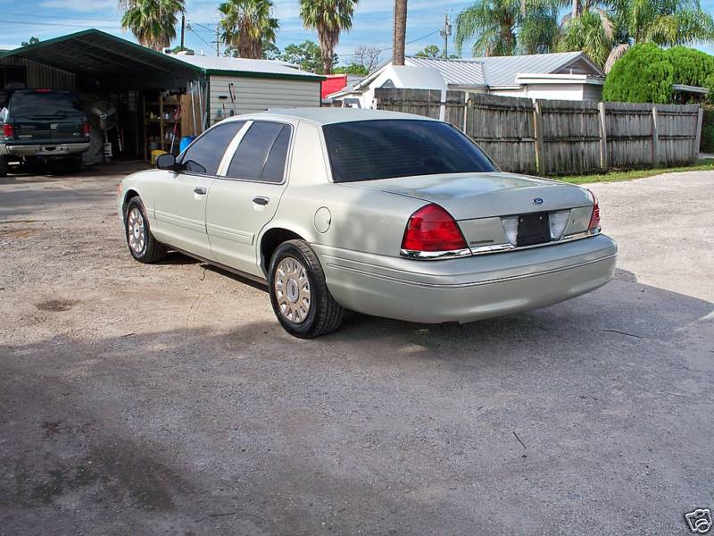 Gold Ford Crown Victoria rear three-quarter view on a gravel drive by a carport