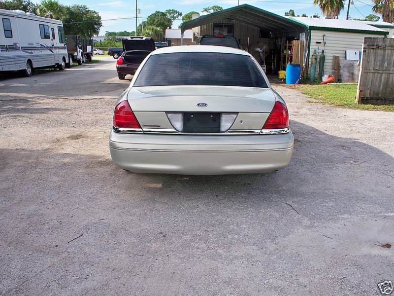 Gold Ford Crown Victoria sedan rear view on gravel lot beside carport