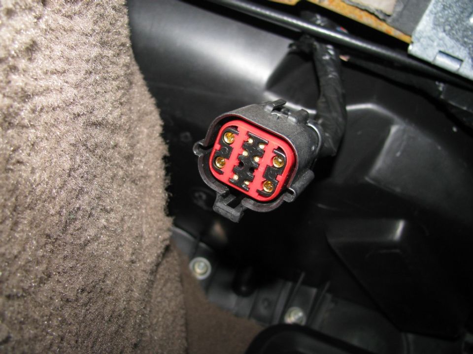 Unplugged multi-pin wiring connector with red insert and gold terminals inside a vehicle