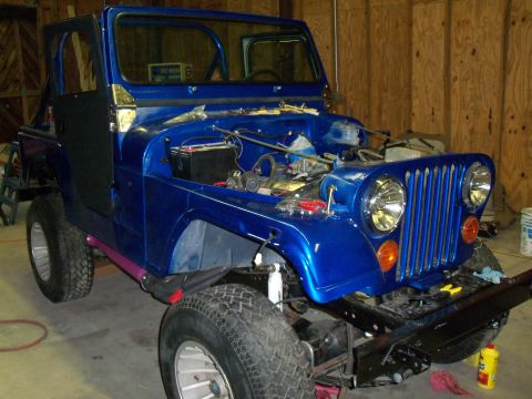 1978 Jeep CJ5 - A blue 1978 Jeep CJ5 is parked indoors with its hood open, revealing the engine compartment and battery.