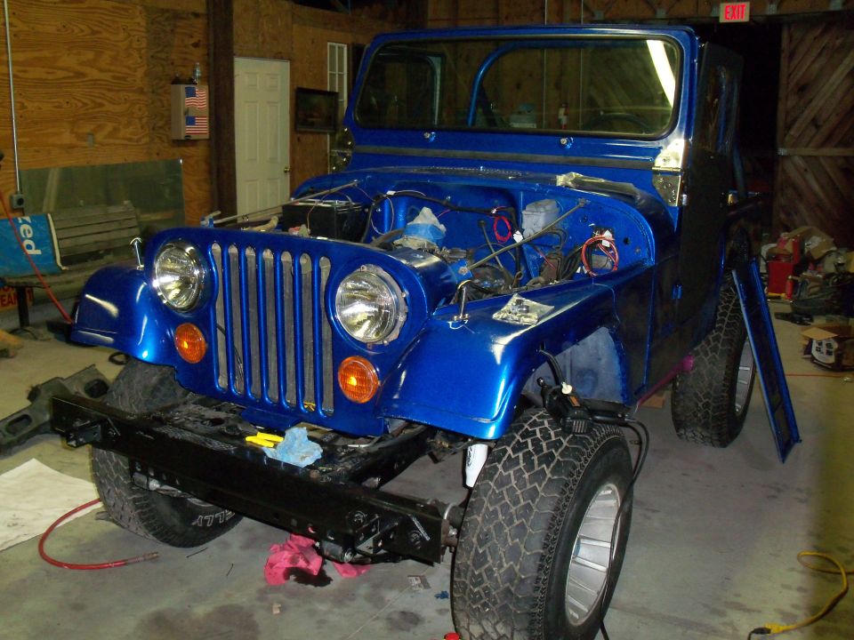 Blue Jeep with hood open, showing engine bay. Front bumper removed