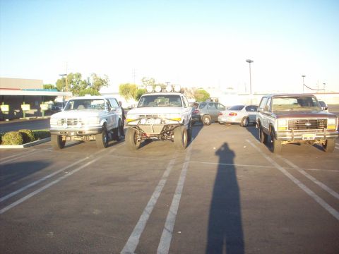 1995 Ford Bronco - Three trucks are parked in a lot under a clear sky.