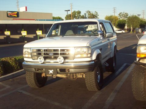 1995 Ford Bronco - A white Ford Bronco is parked in a lot, showing its front grille and headlights.