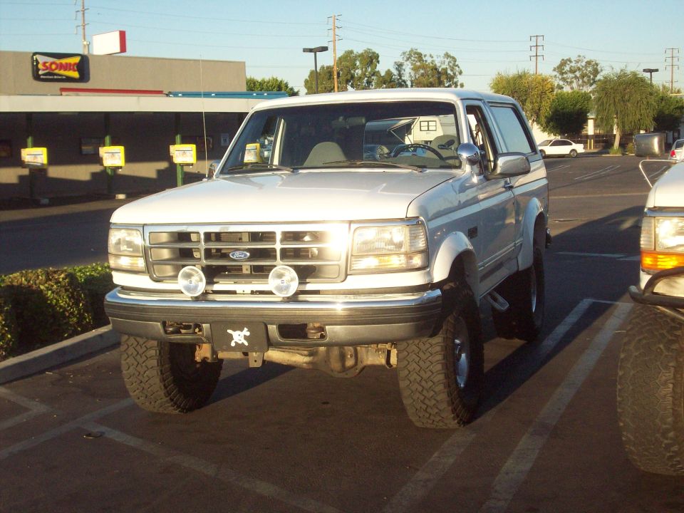 White Ford Bronco front view, parked in a lot. Visible front grille, headlights, and tires