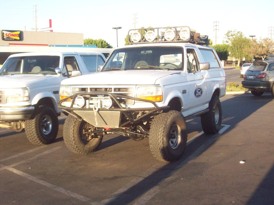 1995 Ford Bronco with custom front bumper, winch, and roof lights parked next to another white Bronco
