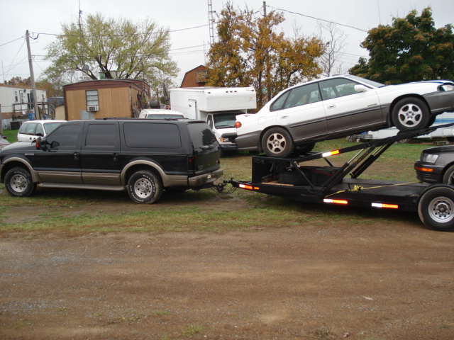 Black Ford Excursion towing a car carrier with a white sedan on it