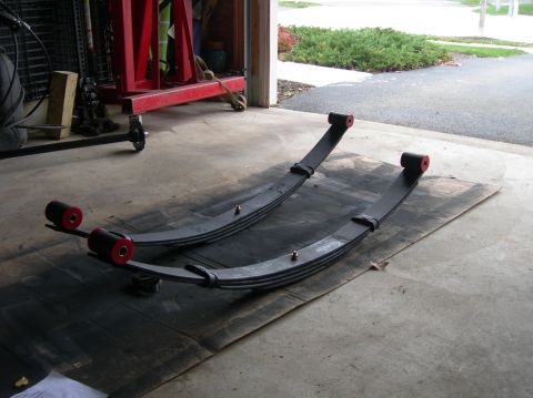1991 Jeep Wrangler - Leaf springs with red bushings are laid out on a mat in a garage.
