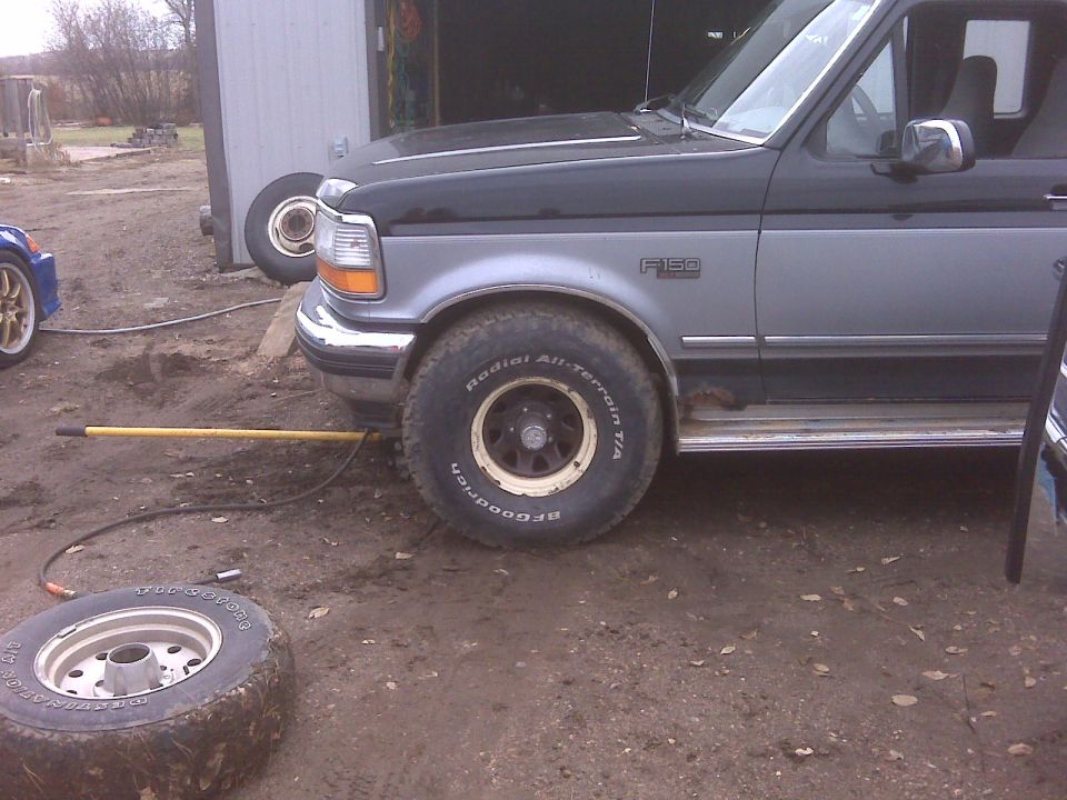 Side view of a two-tone 1994 Ford F-150 pickup truck with off-road tires. Another vehicle is partially visible to the left