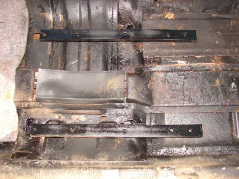 1973 Ford Ranchero - The interior floor of a vehicle shows rust and two black seat mounting rails.