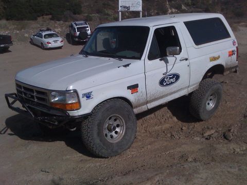 1995 Ford Bronco - This modified Ford Bronco is parked on a dirt lot with other vehicles visible in the background.