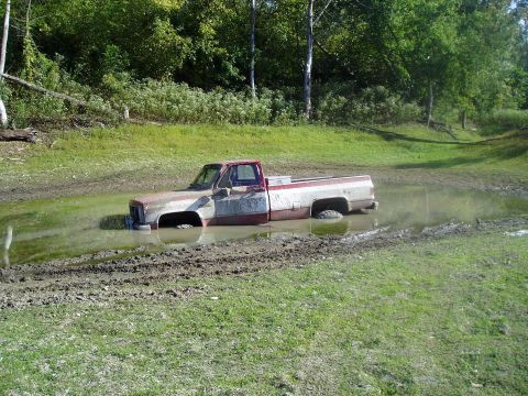 2005 Ford F-150 - A red and white pickup truck is stuck in a muddy puddle with trees in the background.