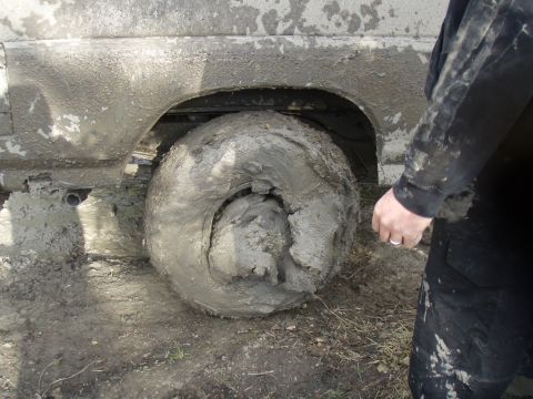 1985 Ford Bronco - A vehicle is deeply stuck in mud, with its tire and lower body heavily covered.