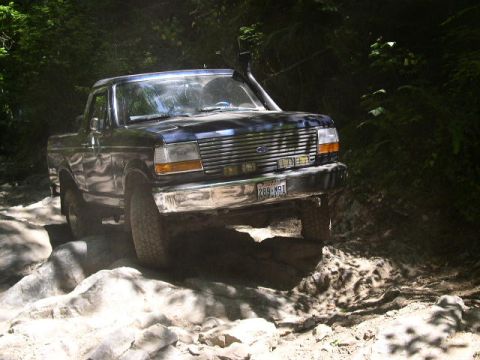1993 Ford Bronco - This Ford Bronco navigates a rocky path through a dense forest, its off-road capabilities.