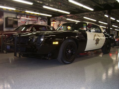 1979 Chevrolet Camaro - A two-tone police car with a push bumper is parked indoors next to another vehicle.