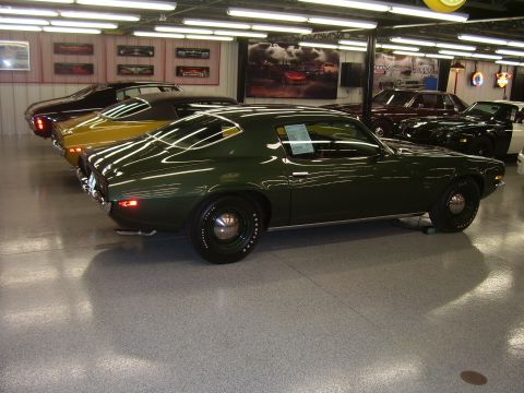 1979 Chevrolet Camaro - A dark green coupe with a black vinyl top is parked in a showroom with other vehicles.