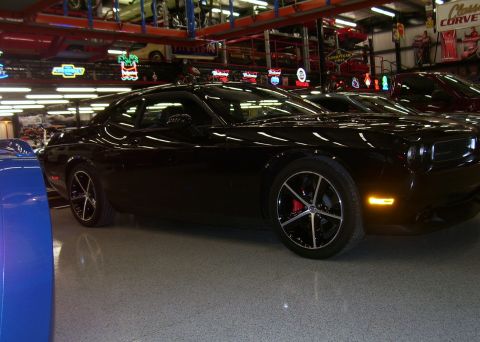 1979 Chevrolet Camaro - A black Dodge Challenger is parked in a garage, alongside other vehicles and memorabilia.