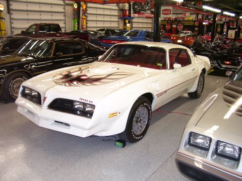 1979 Chevrolet Camaro - A white 1979 Pontiac Trans Am with its iconic hood bird decal and red interior is parked in a garage with other vehicles.