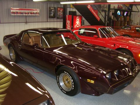 1979 Chevrolet Camaro - A maroon Pontiac Firebird Trans Am is parked in a garage next to a red car.