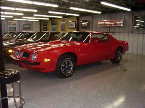 1979 Chevrolet Camaro - Red 1977 Pontiac Firebird Trans Am in a garage setting, parked alongside other vehicles.