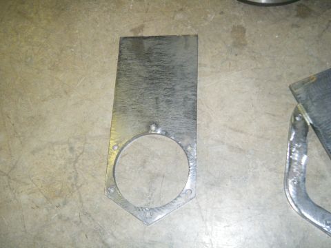 1978 Ford Bronco - A custom metal bracket with a large circular opening and several bolt holes is shown on a concrete floor.