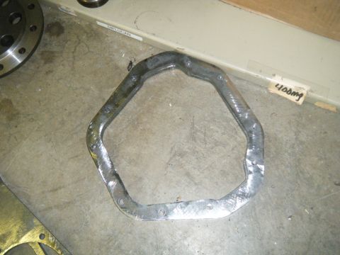 1978 Ford Bronco - Metal part with multiple bolt holes, likely a gasket or flange, on a concrete floor.