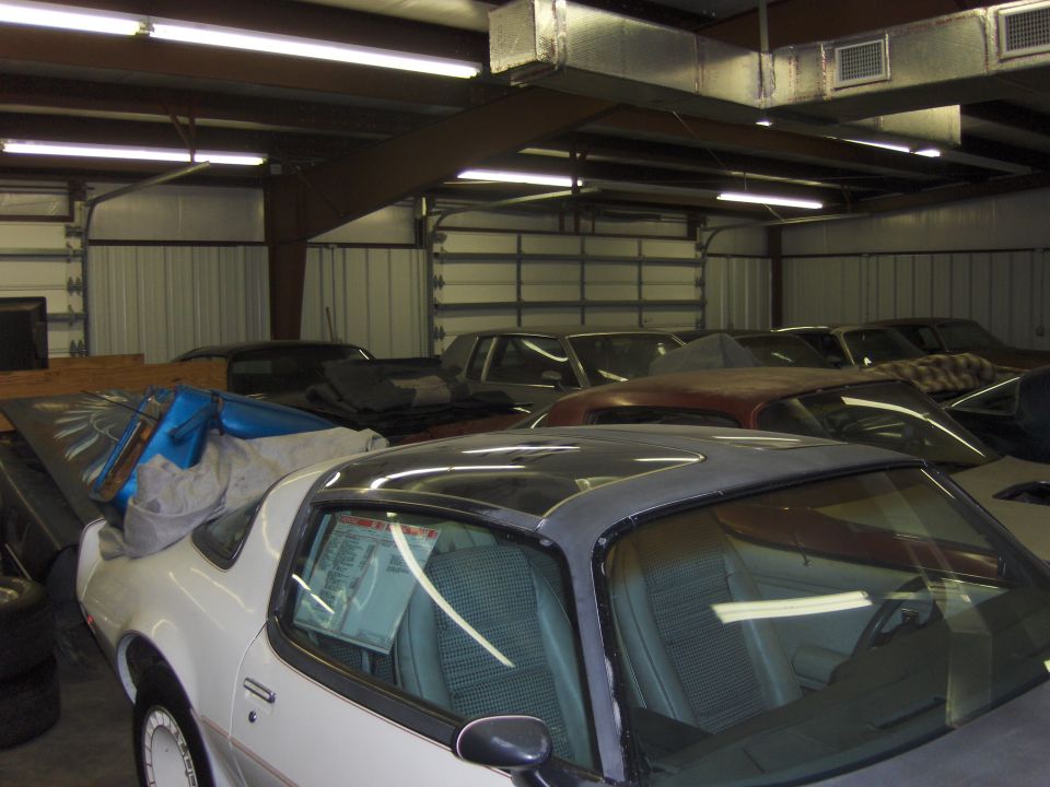 White coupe with black roof, interior visible, parked in garage with other cars