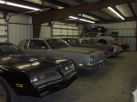 1970 Chevrolet Camaro - Multiple vehicles are stored inside a garage with overhead lighting and large bay doors.