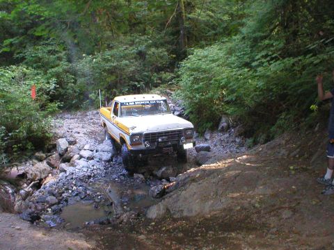 1978 Ford Bronco - A vintage Ford pickup truck navigates a challenging off-road trail with dense foliage surrounding the path.